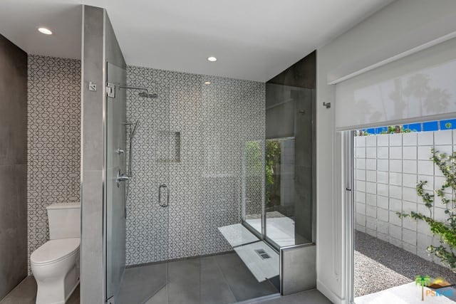 焦点镜头集中在这个世纪中叶的主浴室的步入式淋浴间，有一面时尚的墙壁和灰色的瓷砖地板。