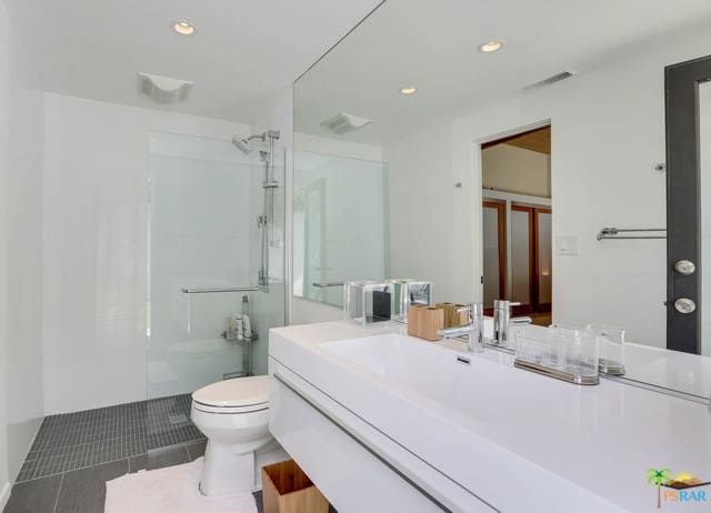 狭窄的中世纪风格主浴室设有白色墙壁和白色浮动洗手池，以及一个小淋浴区。
