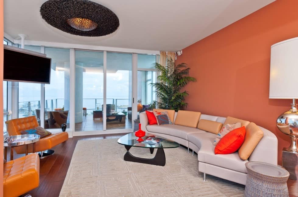 一间柔和的橙色客厅，带有白色的基调，通往阳台。现代时尚的沙发和桌子，暖色调的木地板和灰色地毯为房间增添了个性。
