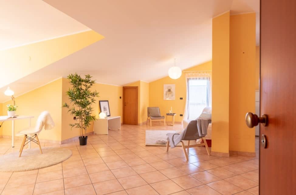 一个现代的开放式客厅，结合了橙色、粉色和黄色的色调，通过使用光线和空间完美发挥。时髦的椅子、桌子、台灯、植物和球形吊灯为房间增添了活力。