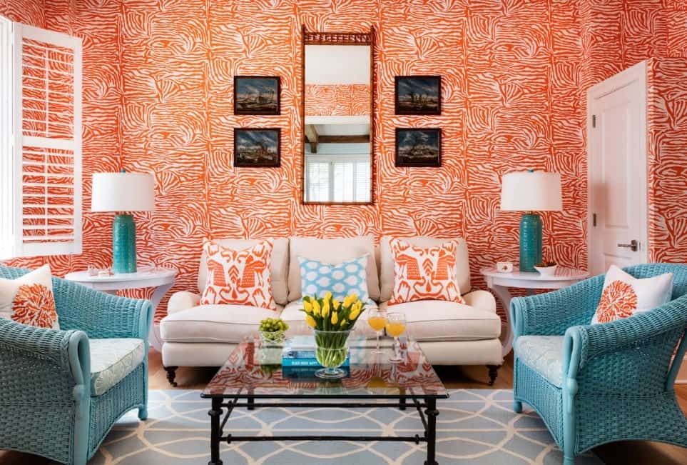 令人愉快的客厅里有充满活力的印花墙壁，舒适的米色沙发，两把淡蓝色藤椅，方形玻璃中心桌，和一张淡蓝色印花地毯。