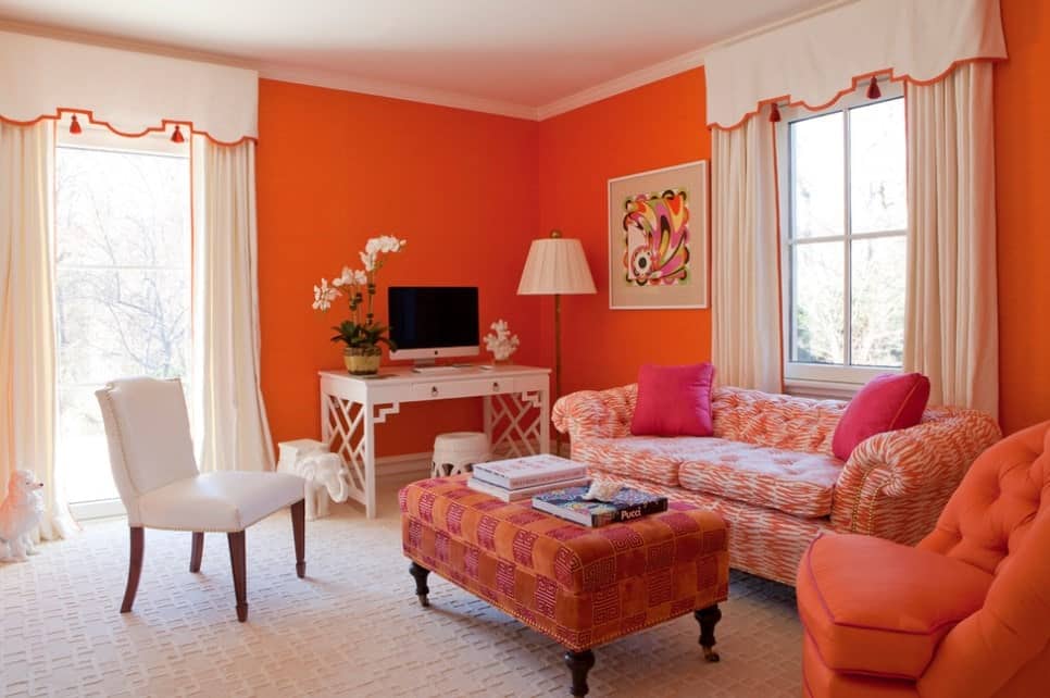 迷人的客厅有橙色的墙壁，橙色的印花沙发，有风格的白色地毯，有软垫的橙色中心桌子，还有一个迷你办公室。