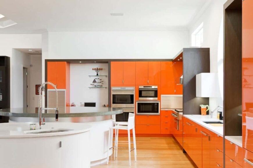 宽敞的现代风格厨房，有闪亮的橙色橱柜，不锈钢电器和两个圆形岛。