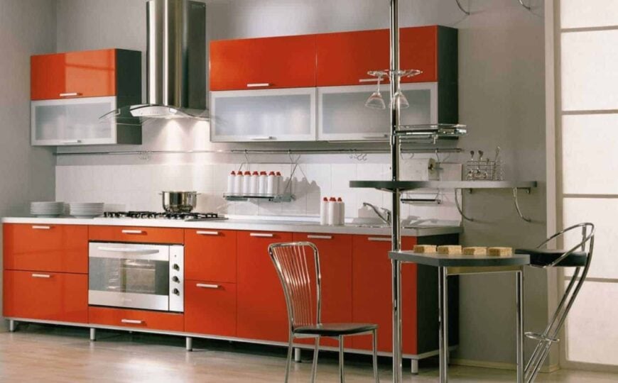 一个单墙厨房，不锈钢电器和不锈钢口音，一个风帽，和焦橙色的橱柜。