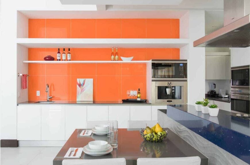 一间带餐厅的厨房，墙壁贴着橙色瓷砖，配有不锈钢用具，地板铺着白色瓷砖。