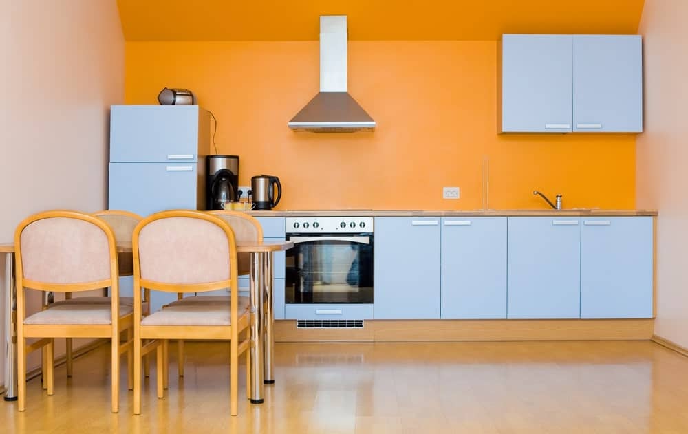 极简主义的墙壁厨房，橙色的墙壁，不锈钢的风帽和电器，浅灰色的橱柜。