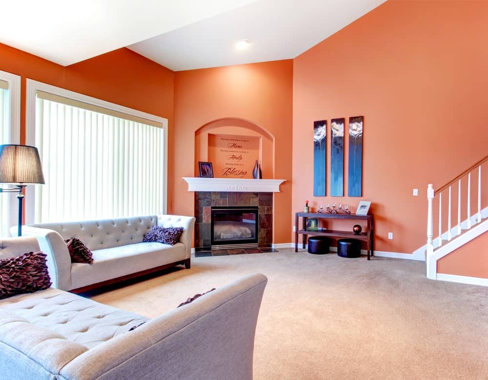 别致的淡橙色地毯的客厅，浅灰色沙发，壁炉，和时尚的枕头。