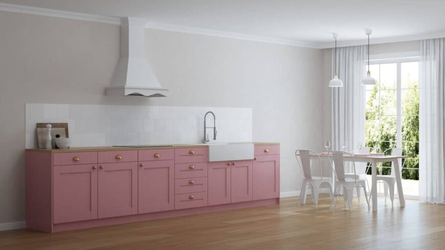 宽敞的厨房设有浅粉色橱柜，木质台面和白色瓷砖后挡板。它包括一个靠近落地玻璃窗的用餐空间。