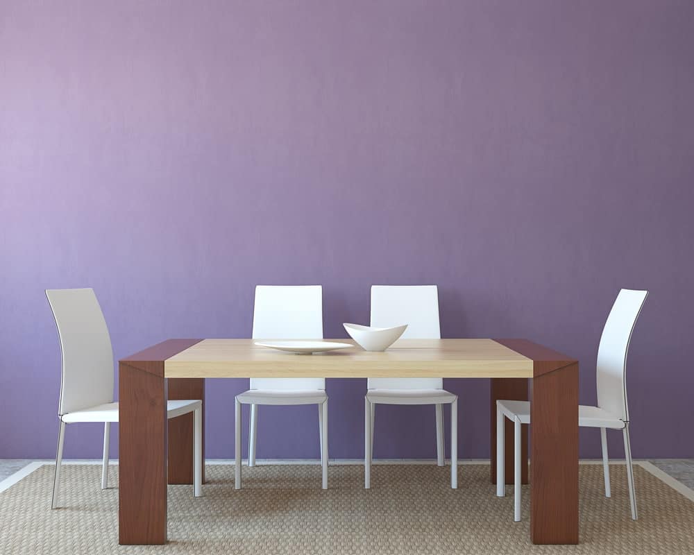 一个极简的餐厅区，淡紫色的墙壁，长方形的四人木桌，白色的椅子，和一个质朴的藤条地毯。