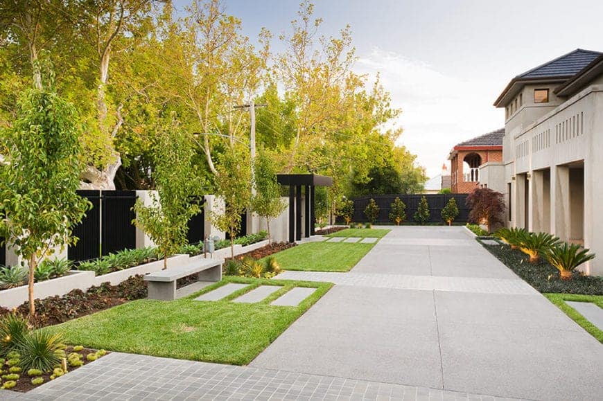 后院有平行的石头小径，穿过绿色的草坪，混凝土长椅，一系列的植物和混凝土植物箱在围墙的一侧。