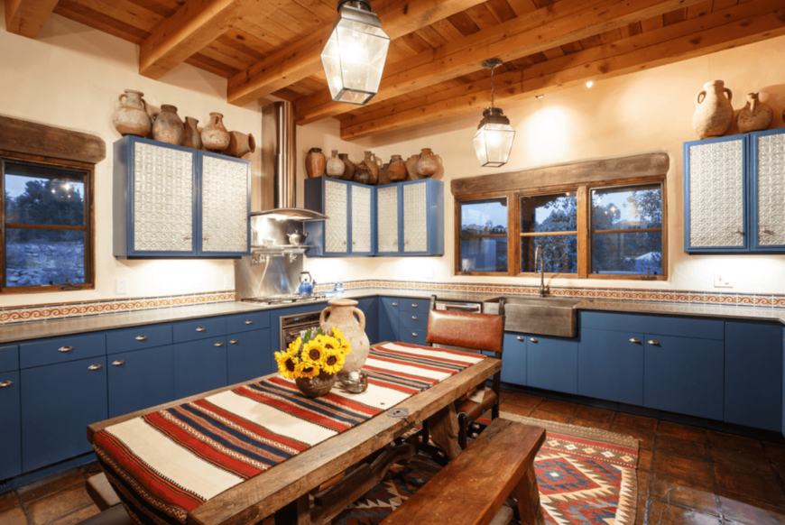 西南厨房设有蓝色橱柜和石板地板。房间里装饰着质朴的陶器花瓶和吊灯。
