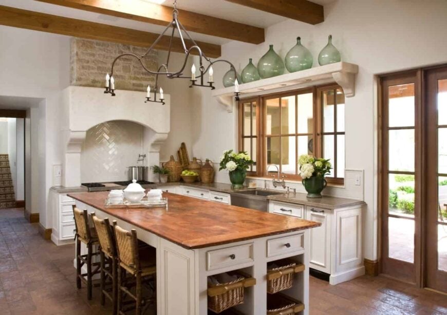 在这间白色的厨房里，锻铁烛台挂在裸露的木梁天花板上。通过玻璃门窗和天窗的帮助，感觉通风明亮。