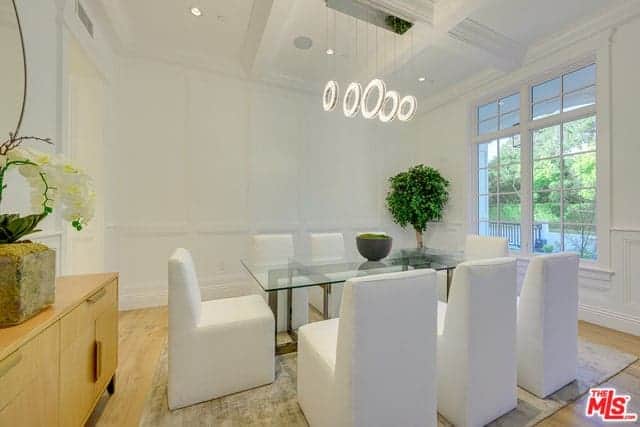 白色的现代椅子与玻璃面餐桌完美搭配，餐桌上有一排现代吊灯，从白色格子天花板上投射出来，映照出高高的白色墙壁。
