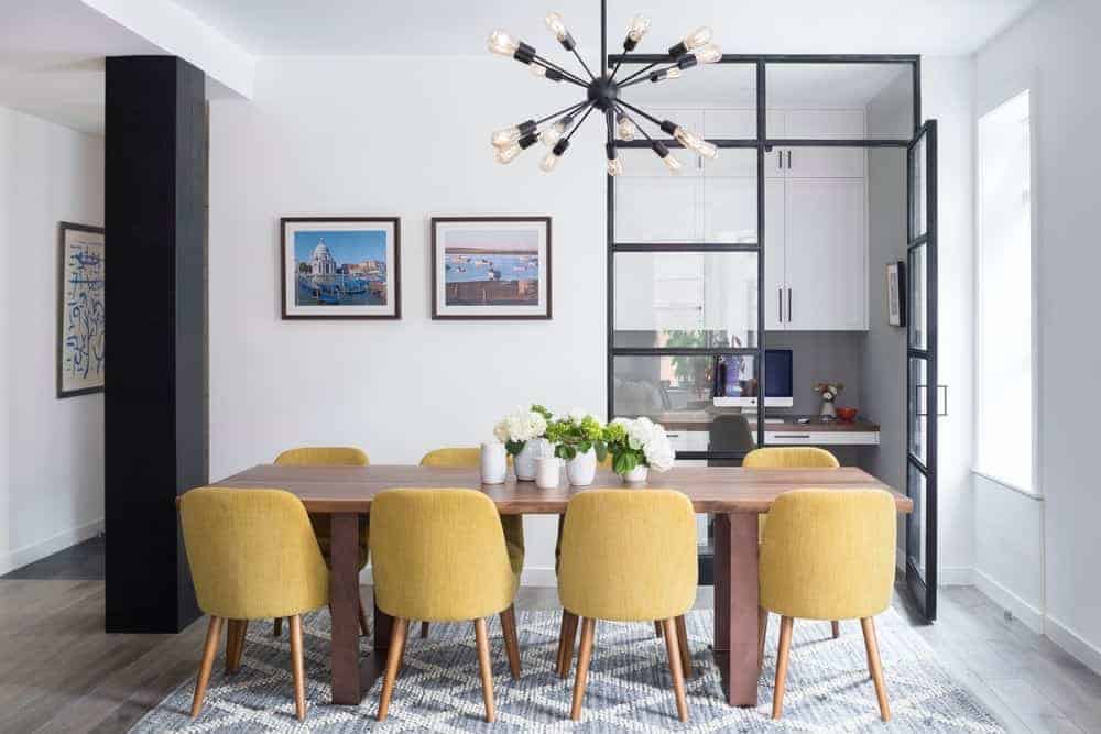 黄色的天鹅绒椅子为餐厅的优雅带来了阳光，现代的Sputnik枝形吊灯悬挂在木桌上，上面是浅灰色的图案地毯。