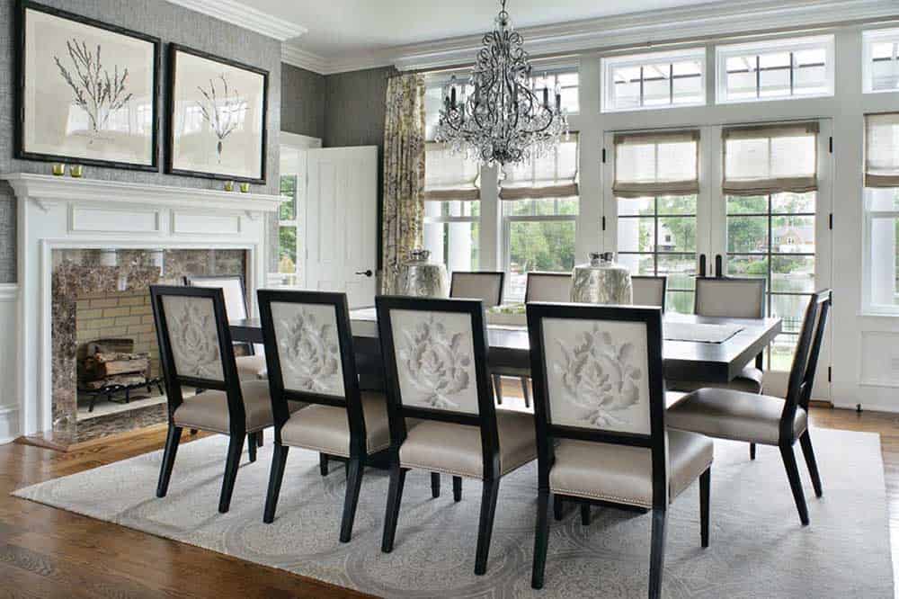 白色和灰色调的餐厅里有一座壁炉、一张长方形木桌、十把椅子和一盏优雅的枝形吊灯。