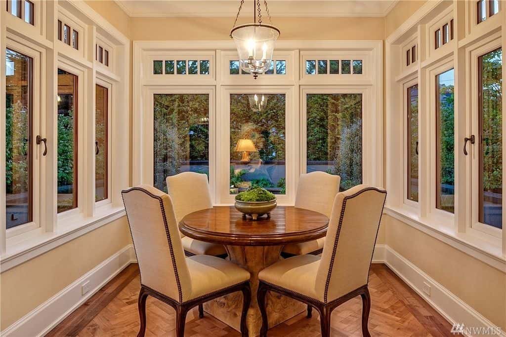 奶油色和白色的墙壁上有一张小圆桌，四把软垫椅子，硬木地板和能看到完美绿地的玻璃窗。