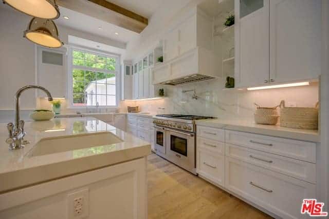 厨房岛台和l形半岛的白色摇床柜和抽屉顶部采用米色大理石，与白色大理石后挡板和硬木地板相辅相成。