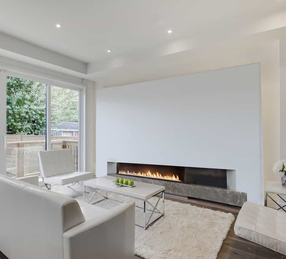 当代客厅区设有一个巨大的壁炉，面对白色对白色的设计元素，包括咖啡桌、地毯、沙发和扶手椅。