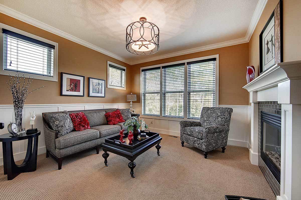这是一间舒适而私密的客厅，铺着地毯的地板与护墙板上方的土黄色墙壁相匹配。与此形成对比的是壁炉对面的沙发和黑色咖啡桌。