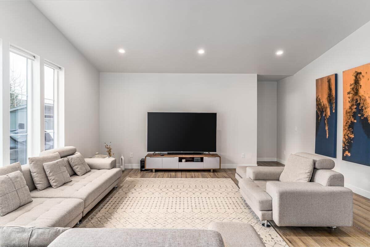 当代客厅设有灰色簇绒沙发，有图案的区域地毯，和一个大电视。大胆、色彩丰富的艺术品为房间增添了独特的色彩。