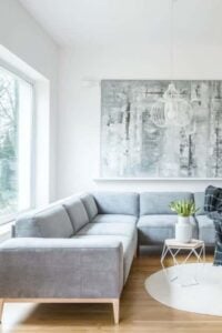 斯堪的纳维亚风格的客厅里有一张灰色的l型沙发，沙发放在靠近玻璃窗的硬木地板上。这个空间还包括一座双面燃木壁炉、采光的大窗户、吊灯和抽象画。