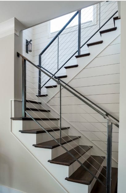 光滑的楼梯配有现代金属栏杆，深色木踏板和白色立管以及白色木板。