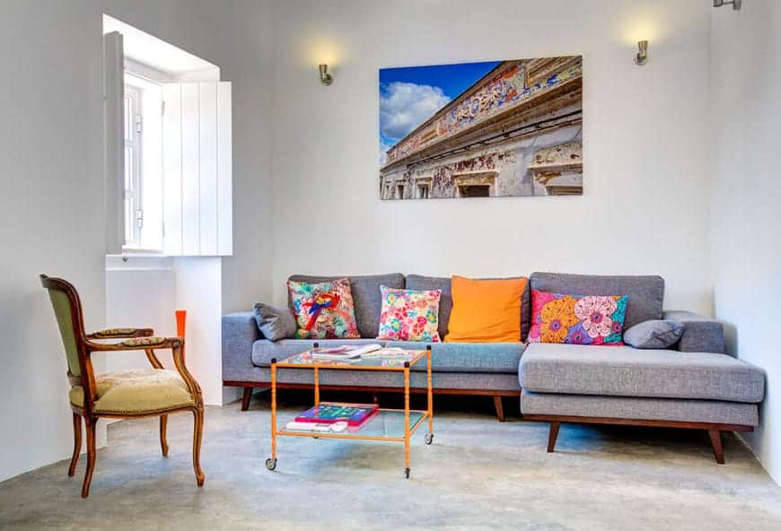 在这间简单的客厅里，一张灰色组合沙发上方挂着一幅可爱的油画。它配有橙色的玻璃咖啡桌和混凝土地板上的软垫椅子。