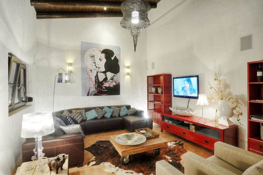 西班牙风格的客厅，有乡村的感觉。它装饰着一件由壁式烛台和工业枝形吊灯照亮的墙壁艺术作品。红色的电视架和架子在这个房间里很显眼。