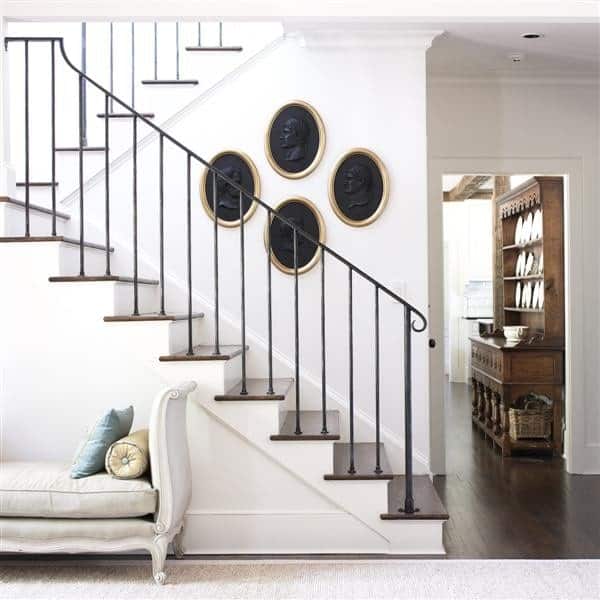 传统的楼梯，手工制作的栏杆和深色木踏板，黑色椭圆形的墙壁装饰。下面是一个优雅的躺椅休息室，上面铺着白色地毯。