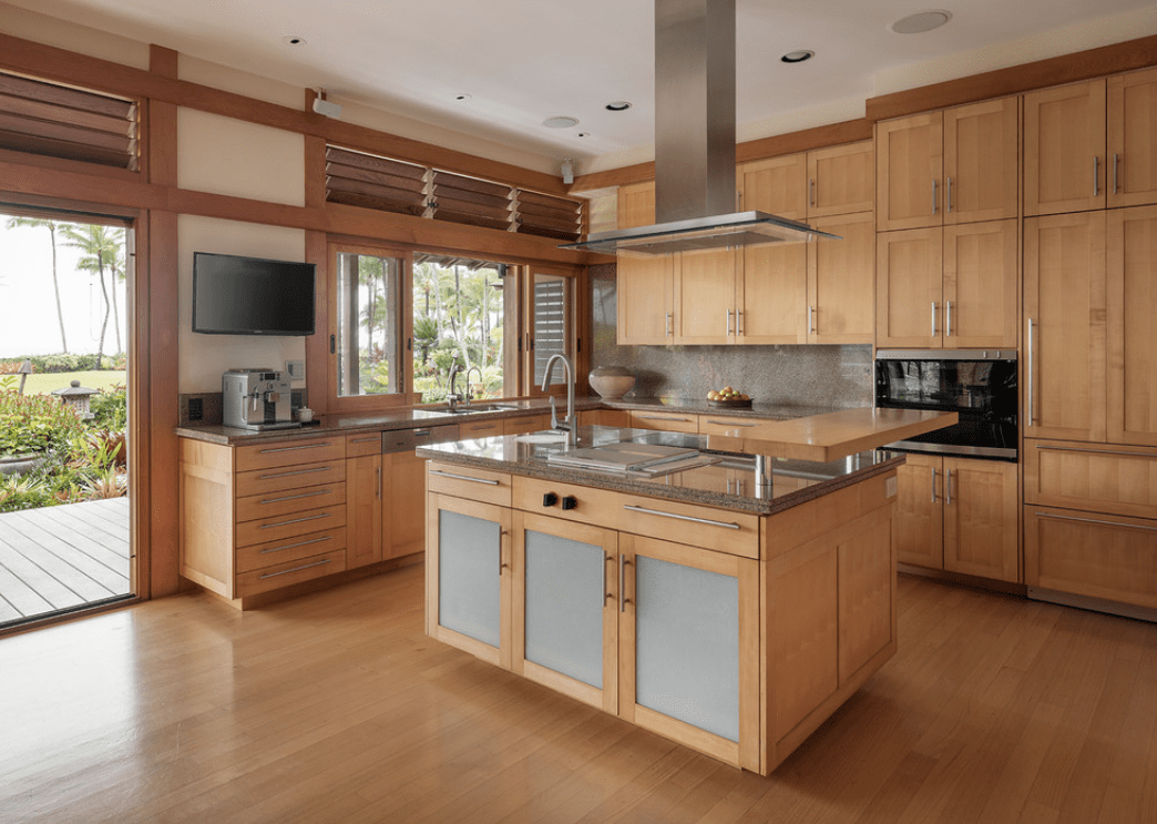 在这个以木材为主题的厨房里，一个不锈钢通风罩位于木制厨房岛上，岛上有灰色大理石和一个凸起的轻质木制柜台。