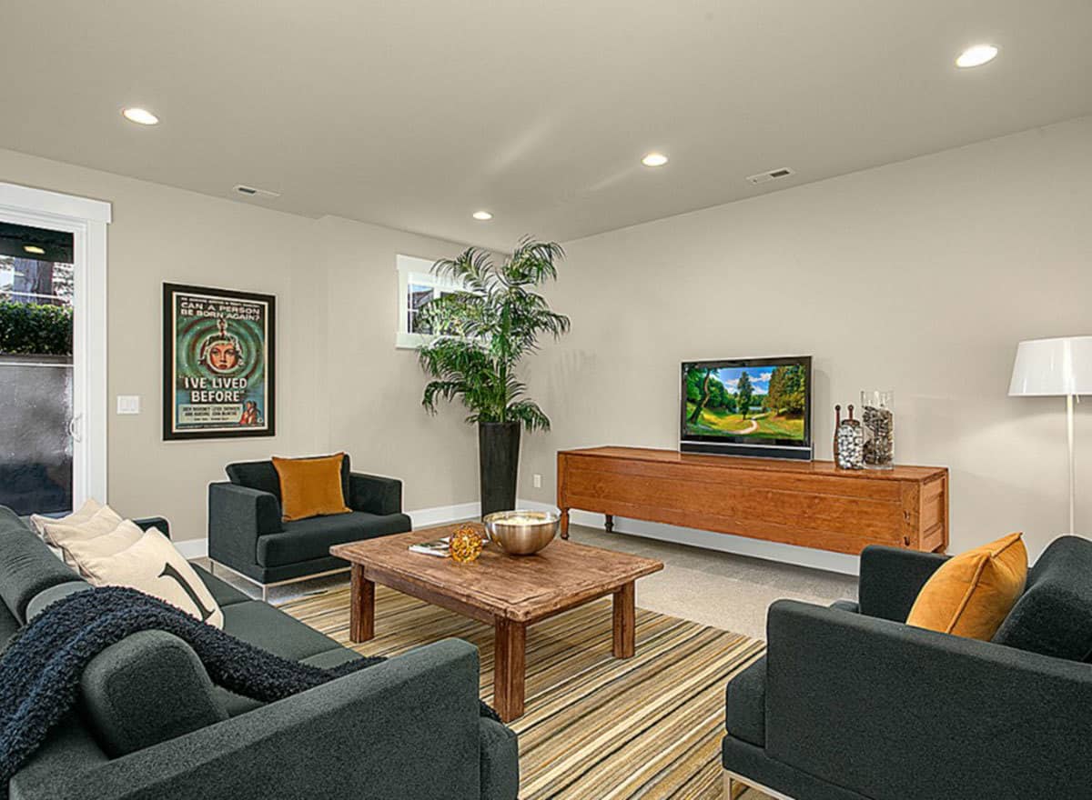 这是一个小客厅，在深灰色沙发组的中间放着木制咖啡桌，角落里有一盆大盆栽。深灰色沙发组与墙壁和天花板的浅灰色色调形成对比。