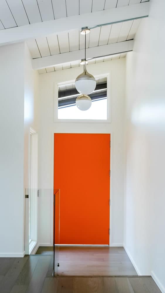 在这条入口通道中，玻璃窗下的一扇亮橙色的门格外显眼。它有一个白色的船型拱形天花板，裸露的木梁和悬挂的球形吊灯。