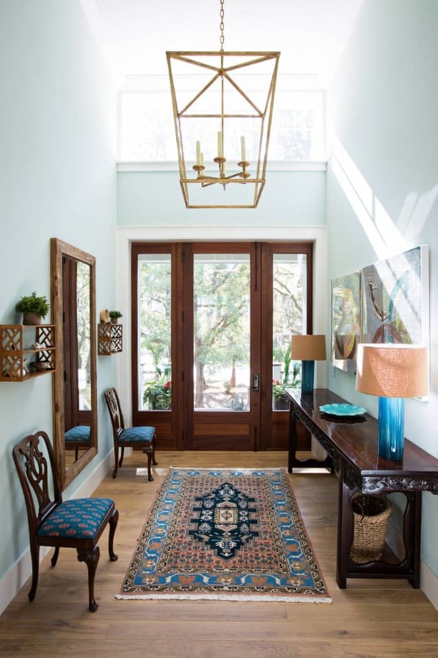 蓝色的门厅与木质家具和地板融为一体。它由一个笼状吊坠和来自玻璃门的自然光照亮。