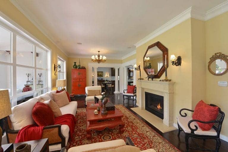 黄色的客厅里，枕头、毯子、地毯和红木咖啡桌点缀着一抹红色。房间里有一面八角形木制镜子下的壁炉，正对着白色沙发。