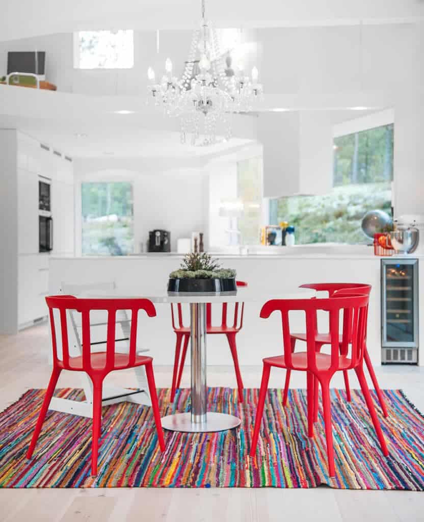 一盏优雅的水晶吊灯照亮了白色的厨房，厨房里有红色的椅子和彩色的地毯。它有一个固定的厨房吧台和一个内置的葡萄酒冰箱。