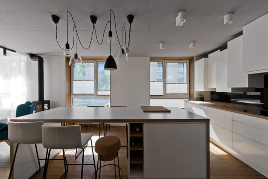 现代厨房由各种风格的吊灯照明，悬挂在白色的厨房岛上，配有内置的酒架。