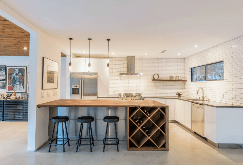 这间厨房的特色是白色地铁瓷砖和一个木制早餐岛，配有一个纵横交错的酒架。