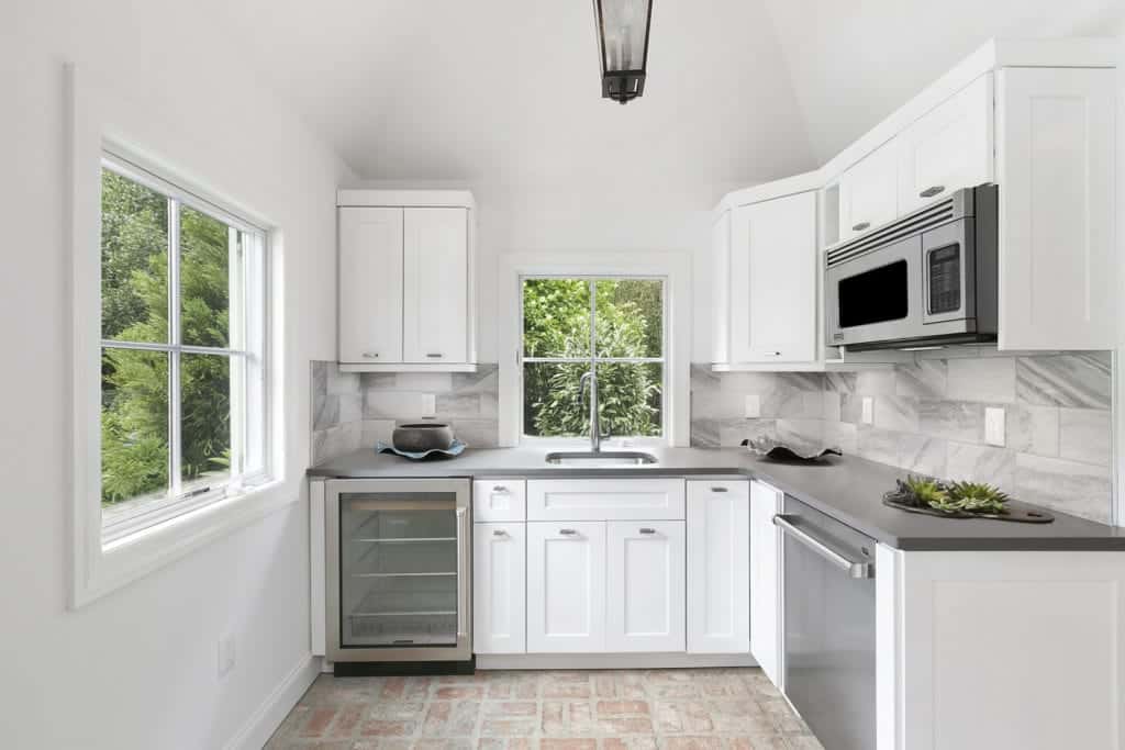 简单的厨房，砖地板和白色橱柜，配有玻璃前葡萄酒冰箱，顶部设有灰色花岗岩柜台。