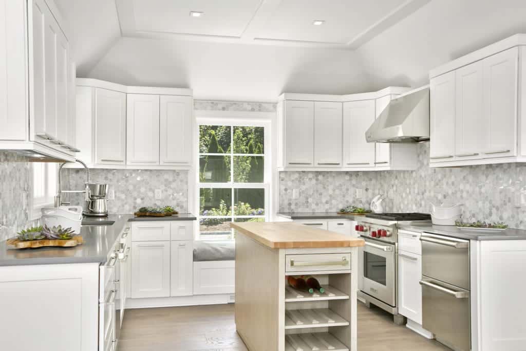 白色厨房与美丽的灰色六边形瓷砖后挡板。它拥有一个固定在框窗下的座位角落，以及带有内置酒柜的轻木早餐岛。