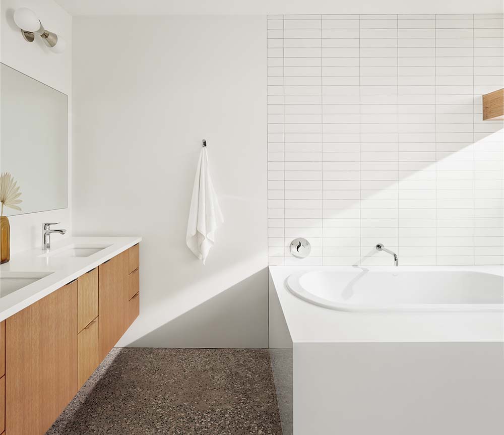 这是一间浴室，墙壁始终是白色的，浴缸的后挡板在灰色地板上的浮动洗手池对面，洗手池上有木制抽屉。