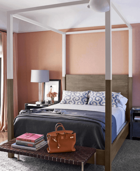 在这个粉红色的主卧室里，近距离观察白色和深蓝色床上用品的天篷床。它与一端的金属长凳搭配在灰色地毯上。
