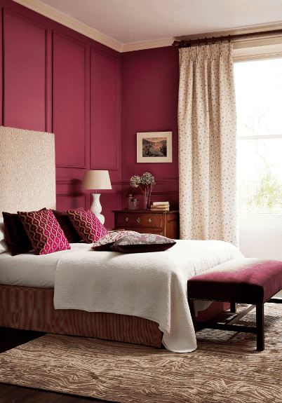 过渡的主卧室以品红的壁板墙和用奶油色窗帘包裹的玻璃窗为特色。它有一张配有几何床头板的床，与枕头相辅相成。