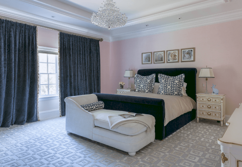 优雅的主卧室展示了淡粉色的墙壁，与藏蓝色的床形成对比，深蓝色天鹅绒窗帘镶有流苏，覆盖着白色框窗。
