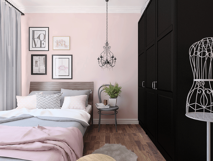 斯堪的纳维亚式的卧室拥有一个黑色的全高衣柜，正对着木床，上面有灰色和粉红色的床品。它装饰着画廊相框和老式枝形吊灯，灰色椅子上放着一盆植物。