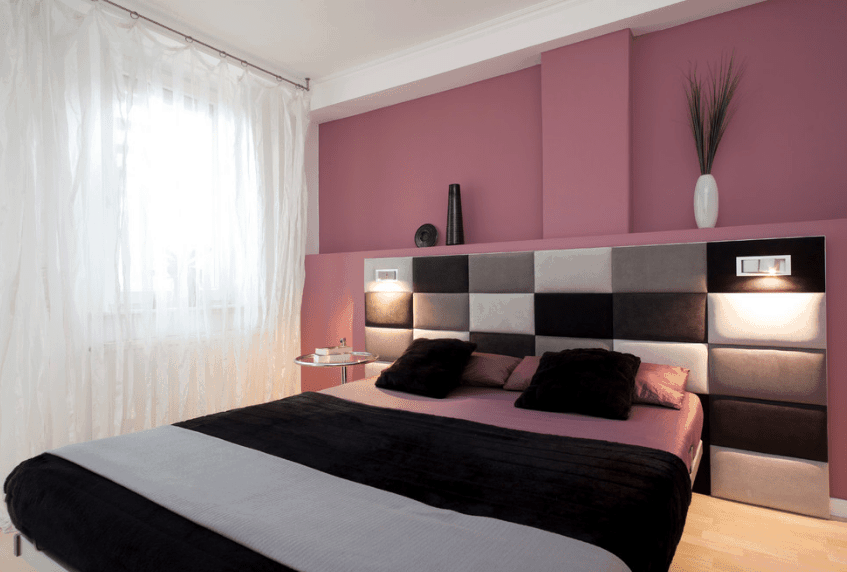 粉红色的主卧室配有一张黑色的床，配有定制的镶板床头板。它有黑色和灰色的面板，装有内置灯。