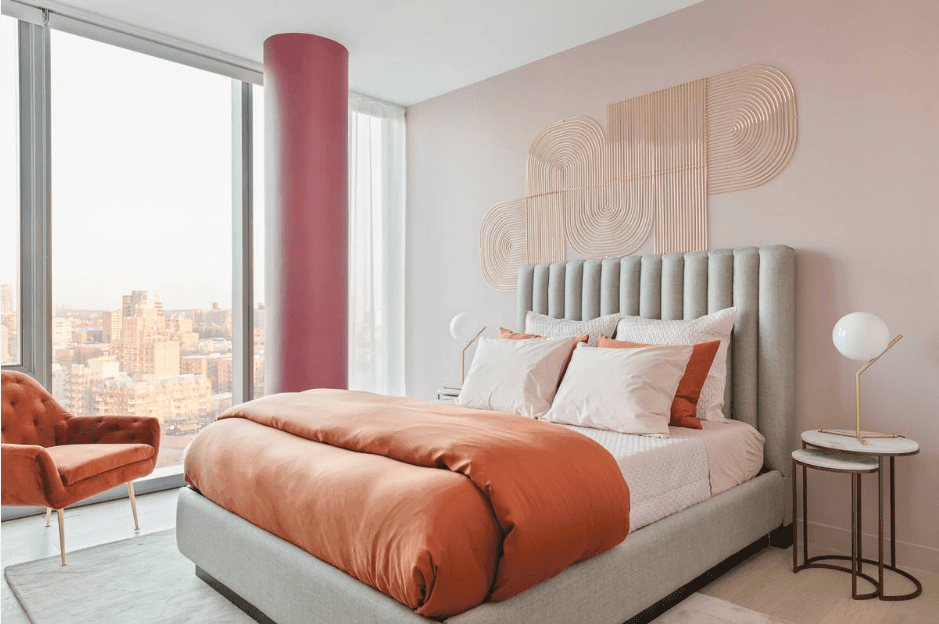 这间主卧室拥有铜粉色的墙壁艺术和通高的玻璃，俯瞰着令人惊叹的城市景观。