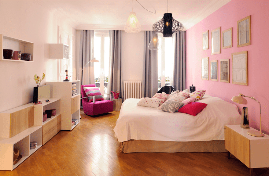主卧室设计有各种风格的吊灯和画廊框架安装在粉红色的墙壁上。