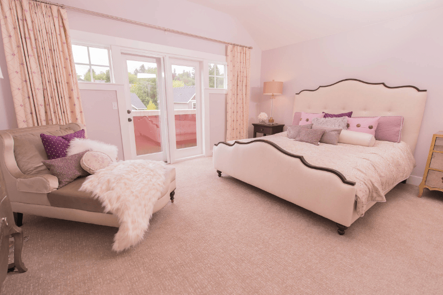 在这个粉红色的主卧室里，一张灰色的躺椅，上面有彩色的枕头和毛皮毯子，正对着可爱的白色床。