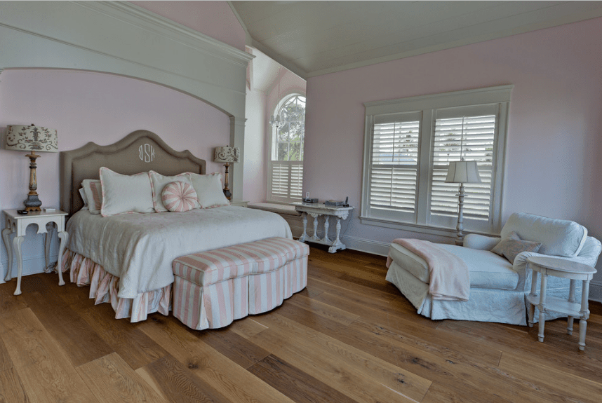 工匠的主卧室，白色和粉红色的床，配有棕色软垫床头板，硬木地板上配有白色躺椅。