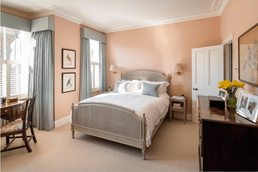 舒适的卧室以藤条床为特色，由壁灯和自然光线从覆盖在灰蓝色窗帘的玻璃窗。